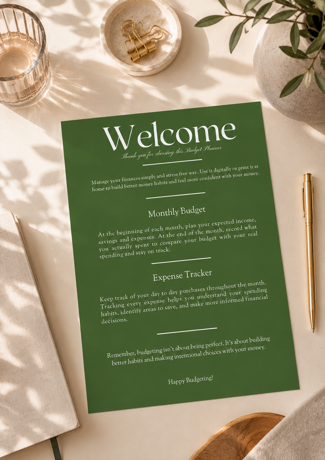 A green printable budgeting and expense tracker card styled in a flat lay with a notebook, gold pen, glass, and decorative bowls on a light beige surface.