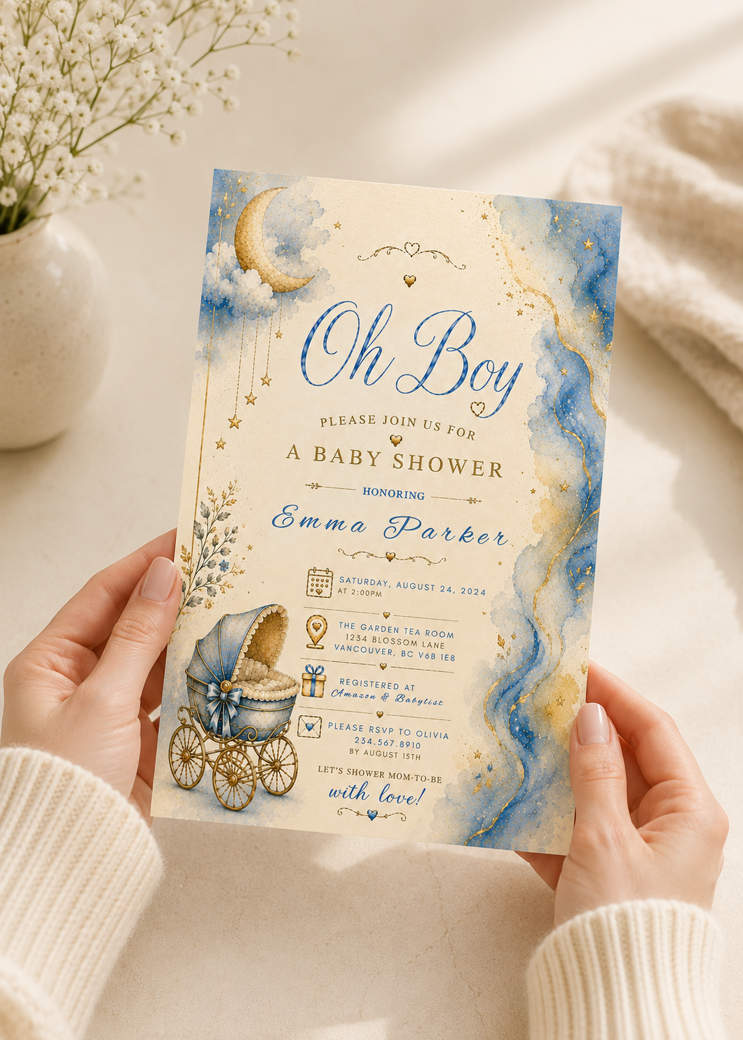 A person holds a baby shower invitation card featuring a whimsical watercolor design with blue and gold marbled patterns, a crescent moon, stars, and an illustration of a baby carriage. The card reads 'Oh Boy Please Join Us For A Baby Shower Inviting Emma Parker'.