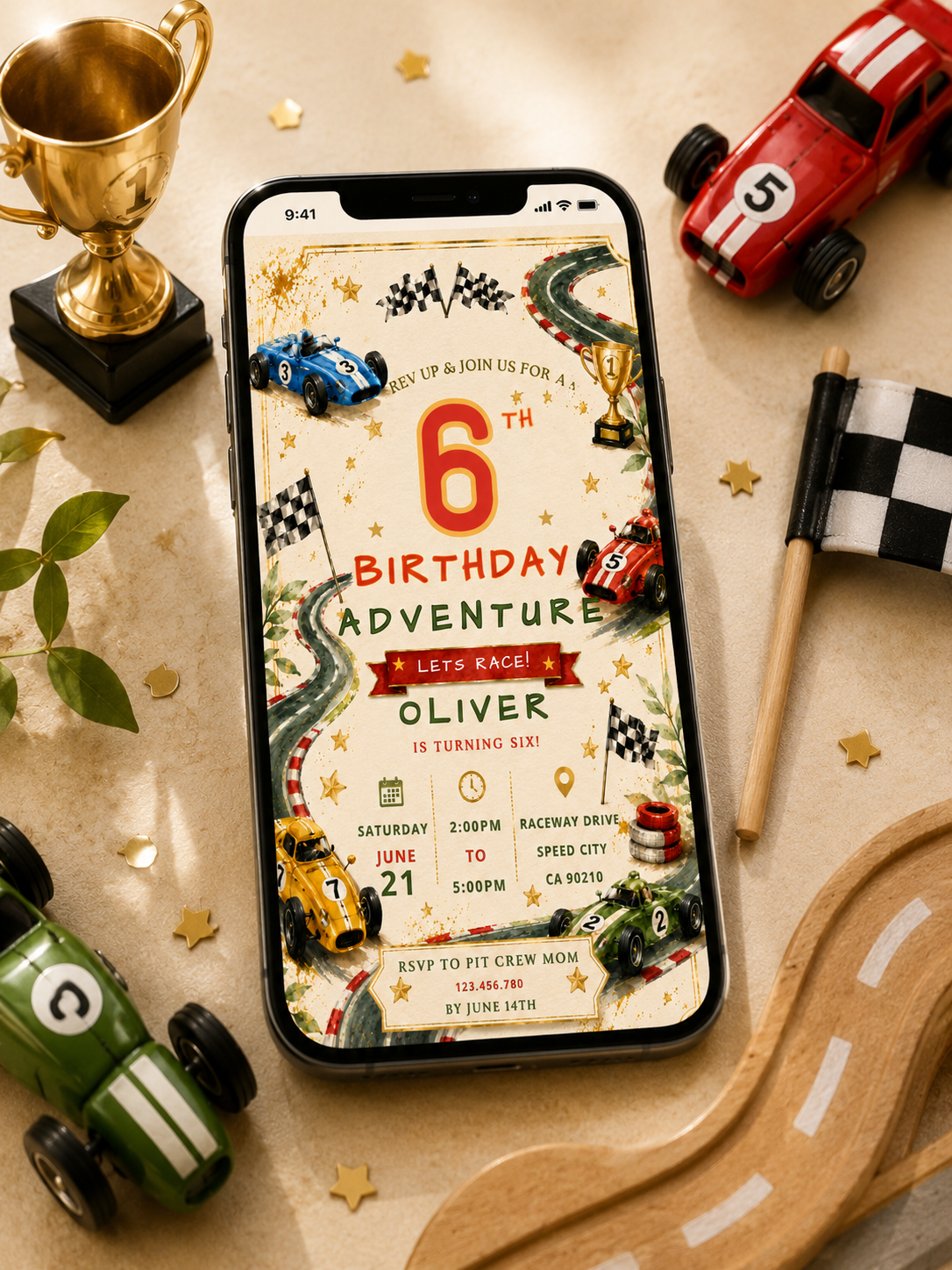 A smartphone displaying a 6th birthday race-themed invitation card, styled on a beige tabletop with toy race cars, a trophy, a checkered flag, and a wooden race track.