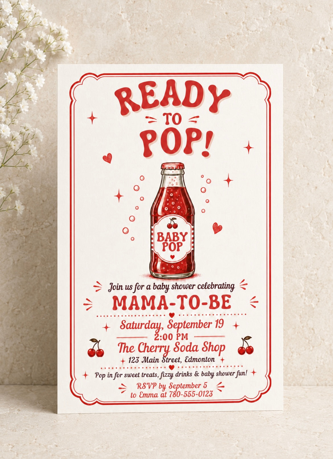 A baby shower invitation card featuring a retro red and white design with the text 'READY TO POP!' and an illustration of a baby soda bottle, displayed on a textured beige background with small white flowers.