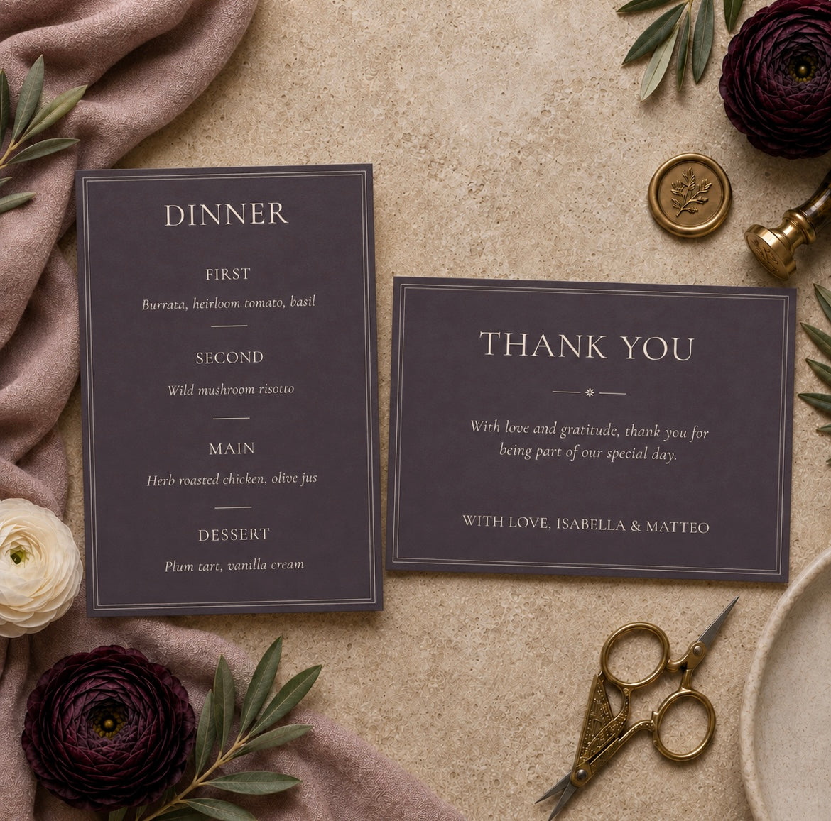 A styled flat-lay of a dinner invitation and matching thank you card on a textured beige surface, surrounded by dark purple flowers, green leaves, a blush fabric napkin, gold scissors, and a gold wax seal.