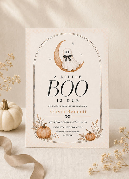 A baby shower invitation card with a Halloween theme, styled on a neutral beige surface with dried flowers, a small white pumpkin, and a beige ribbon. The card features a ghost on a crescent moon, the text 'A LITTLE BOO IS DUE', and autumn pumpkins at the bottom.
