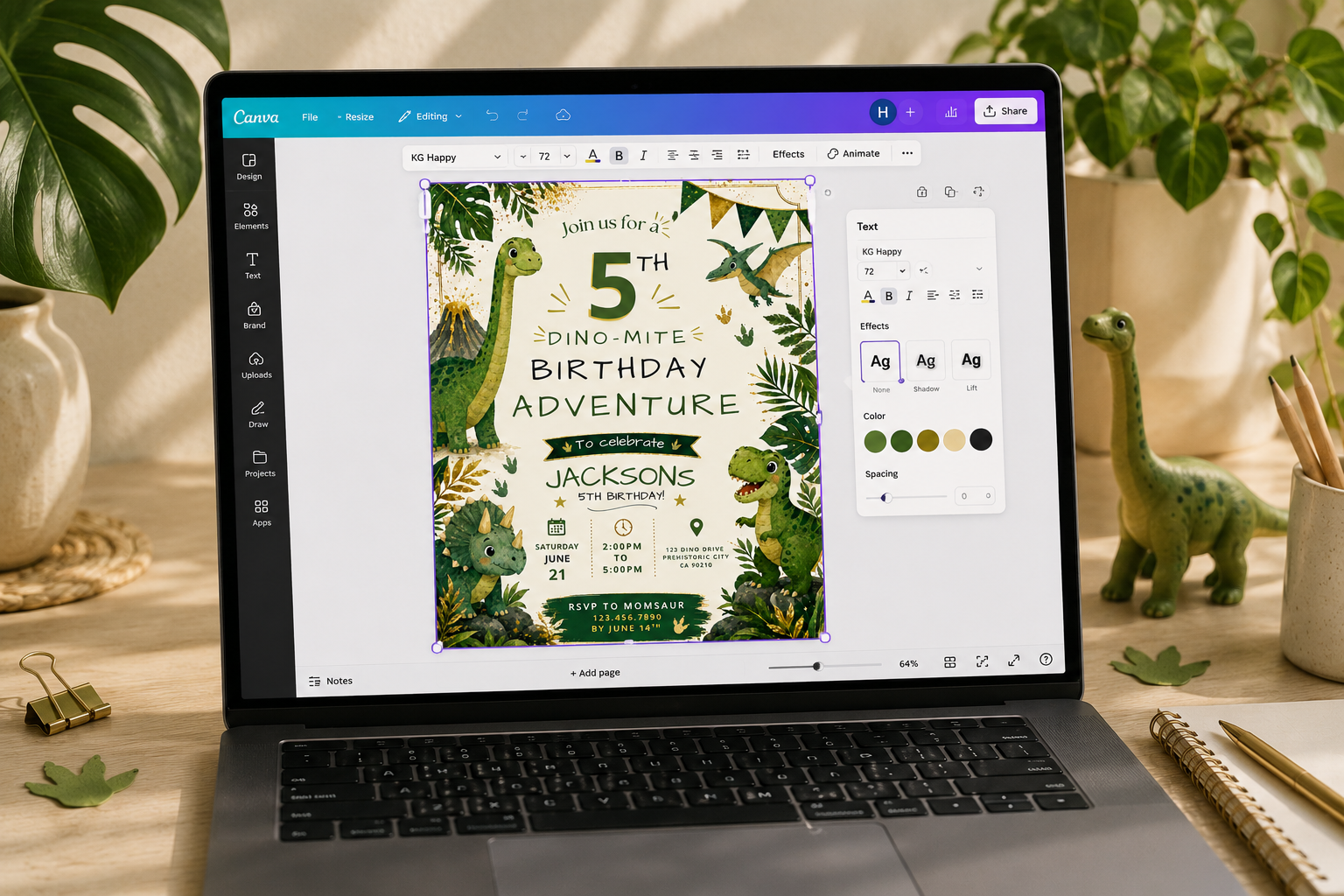 A laptop on a wooden desk displaying a dinosaur-themed birthday invitation design. The scene is styled with potted plants, a small green dinosaur figurine, and stationery.